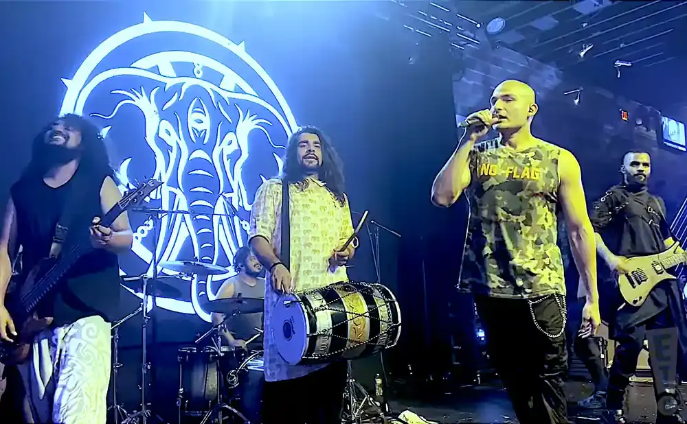 A band performs on stage with a large blue elephant logo behind them.