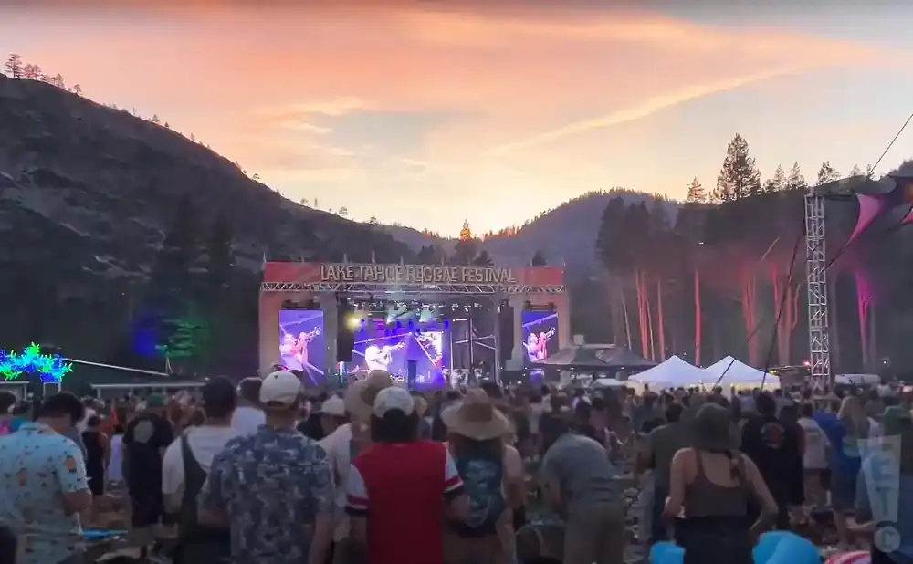 Crowd at Lake Tahoe Reggae Festival at sunset with mountains and a stage.