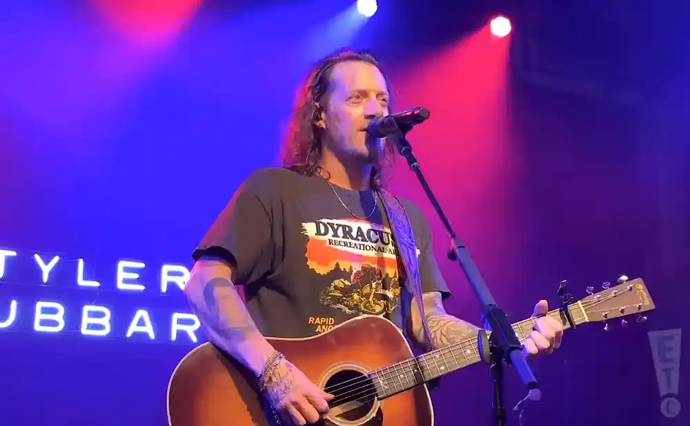 Musician Tyler Hubbard plays guitar and sings on stage with blue and pink stage lighting.