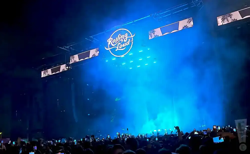A large outdoor concert crowd under a blue-lit stage with a 