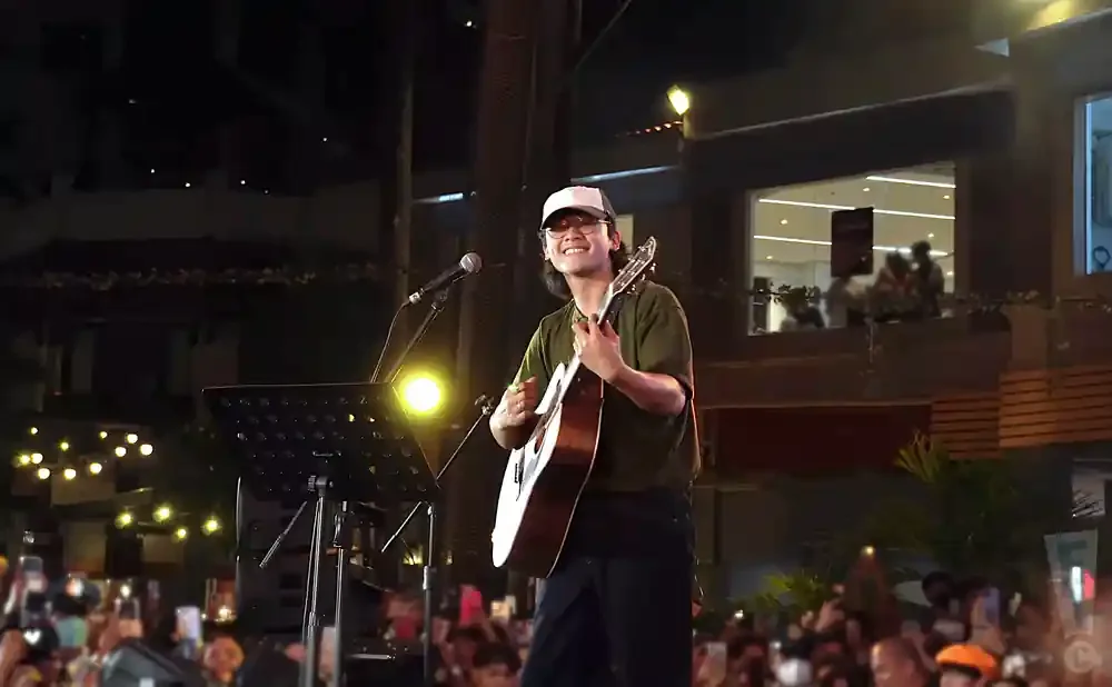 A man in a cap and glasses plays an acoustic guitar on a stage at night.