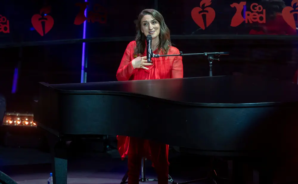 A woman in a red dress sings into a microphone in front of a piano, with a 