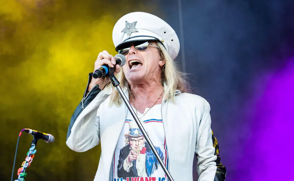 A male singer in a white hat and jacket sings into a microphone with a 