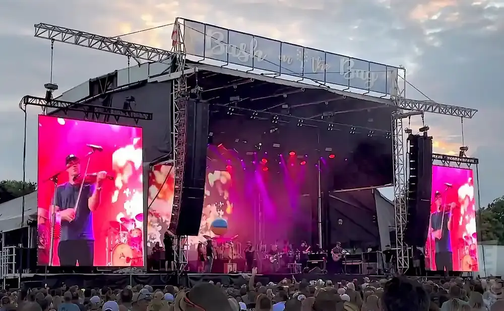 A concert stage with large LED screens showing a violinist.
