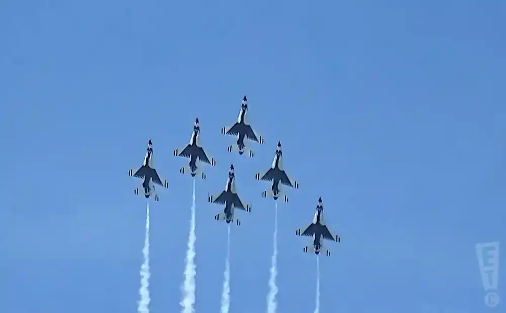 Six Thunderbirds jets fly in formation against a clear blue sky, leaving white smoke trails.