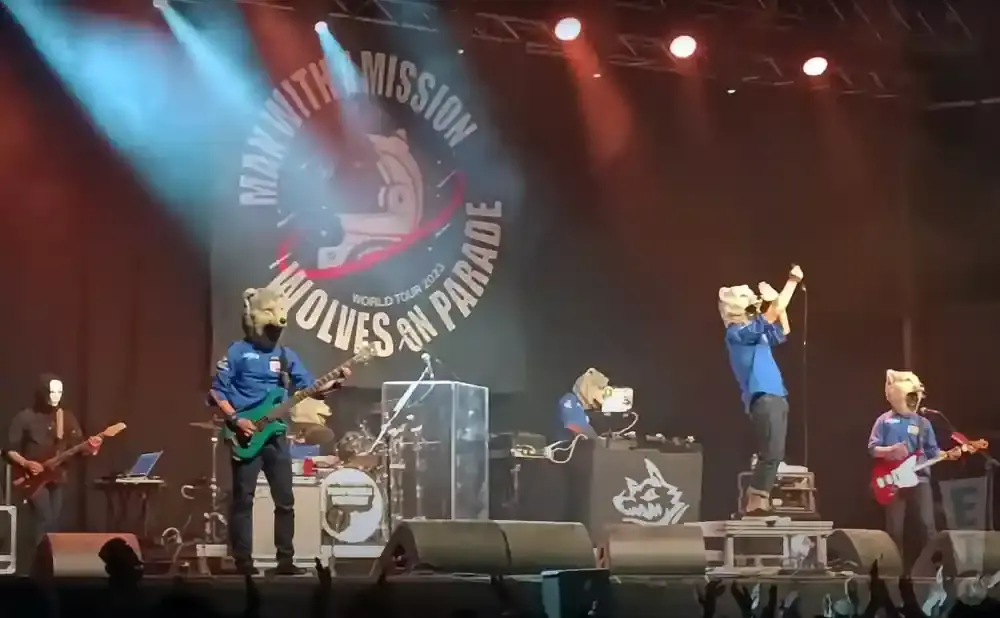 Band members with wolf masks perform on stage, with a banner in the background reading 