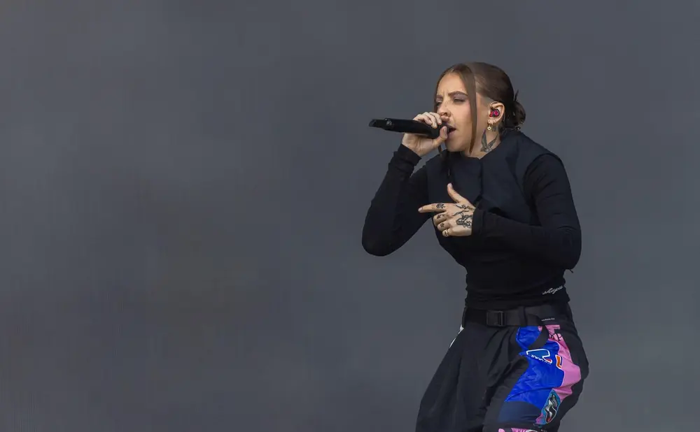 Rapper performing on stage, wearing a black top and colorful pants.