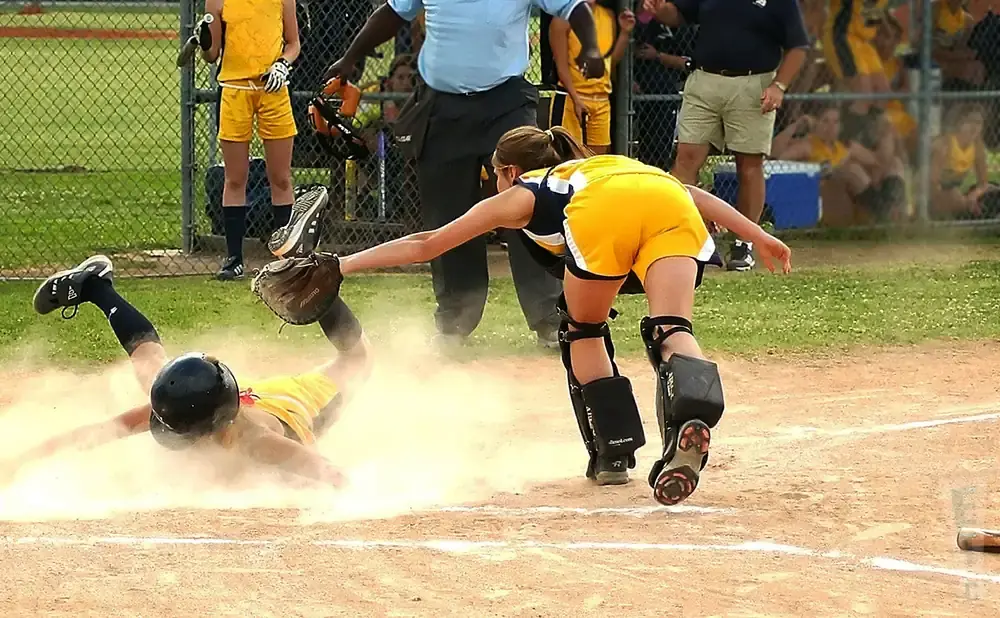 A softball player slides into home plate as the catcher attempts a tag.