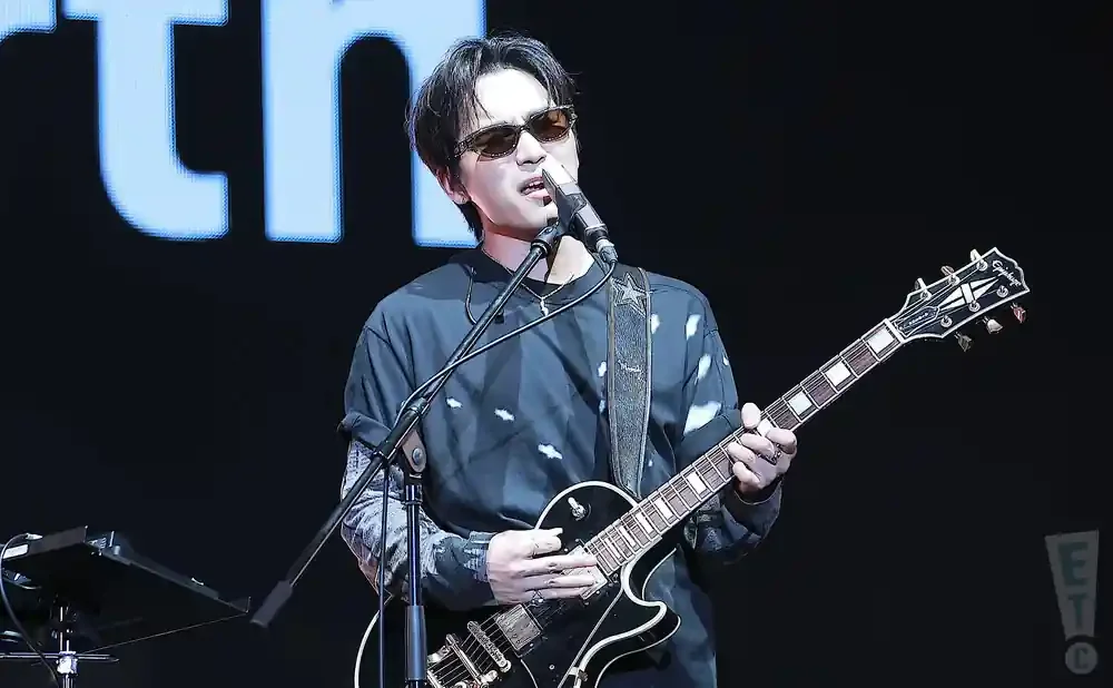 A man in sunglasses sings and plays an electric guitar on stage.