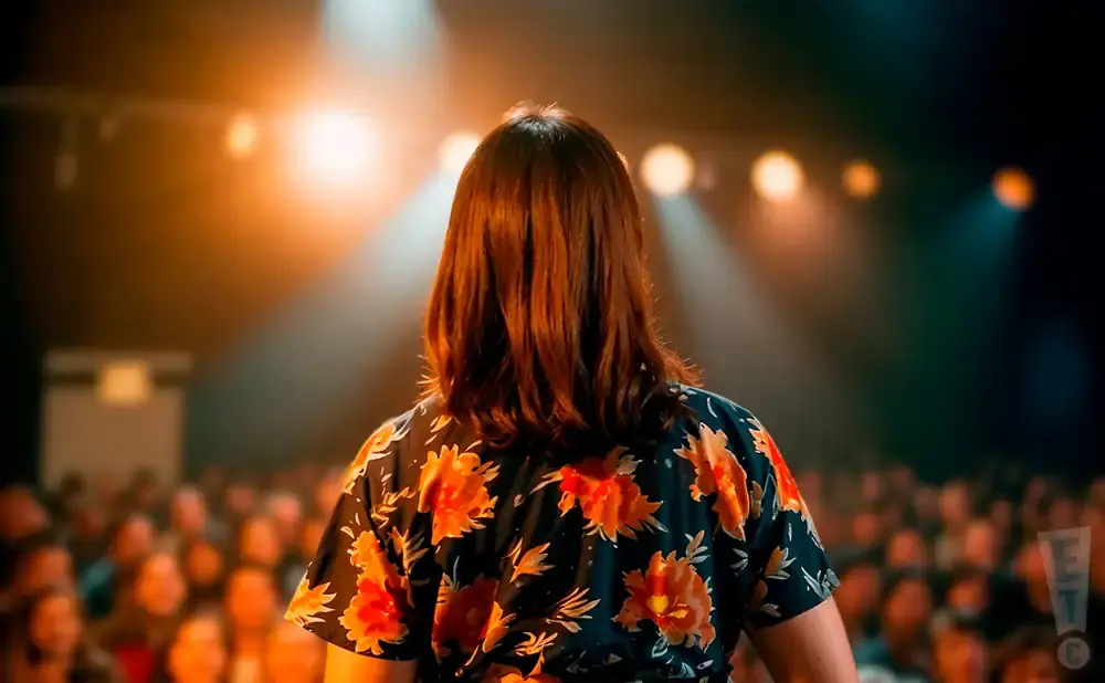 Person in a floral shirt on stage with audience and lights
