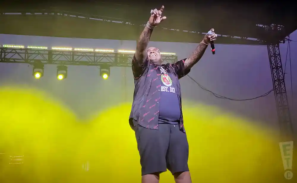 A male performer on stage with his arms raised, holding a microphone.