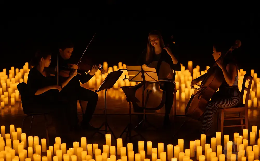 Four musicians play instruments surrounded by a sea of flickering candles.