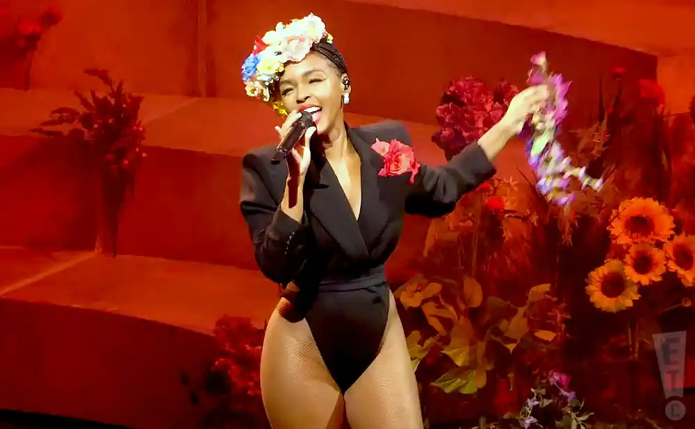 Singer Janelle Monáe performs in a black leotard and blazer, wearing a flower crown and holding a bouquet.