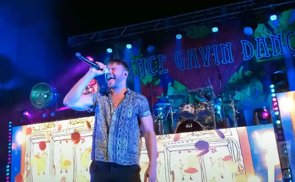 A male singer on stage at a concert, holding a microphone and singing.