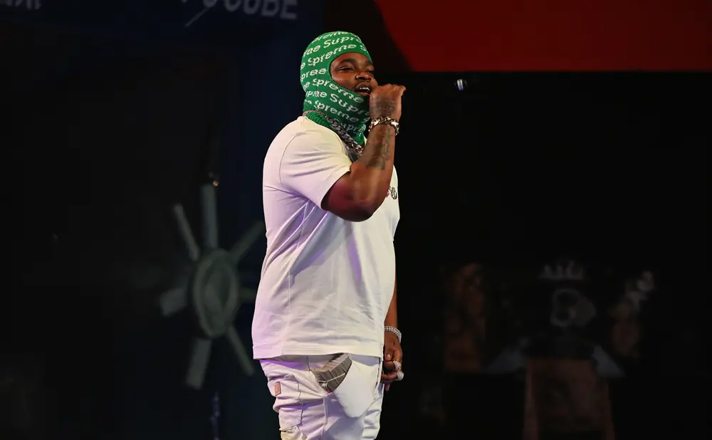 Rapper with a green balaclava and white outfit, holding a microphone.