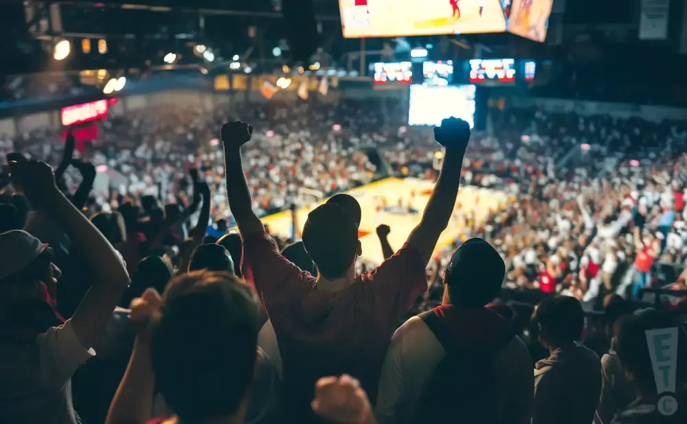 Crowd of fans cheering with fists raised at a sporting event.
