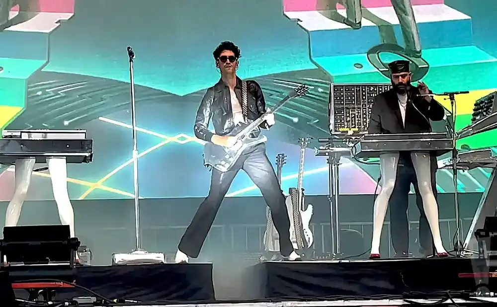 Two musicians perform on stage with guitars and keyboards.