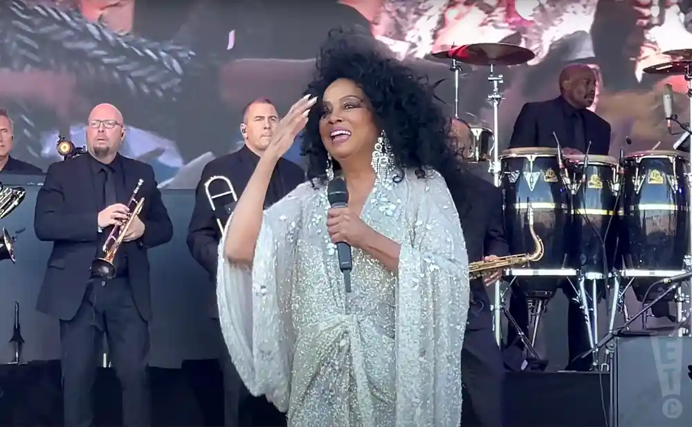 Diana Ross sings on stage in a sparkly gown, accompanied by a band with horns and percussion.