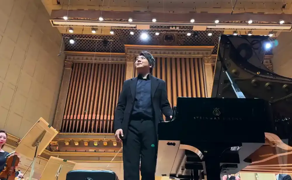 Pianist looking up by a Steinway grand piano in a concert hall with organ pipes.