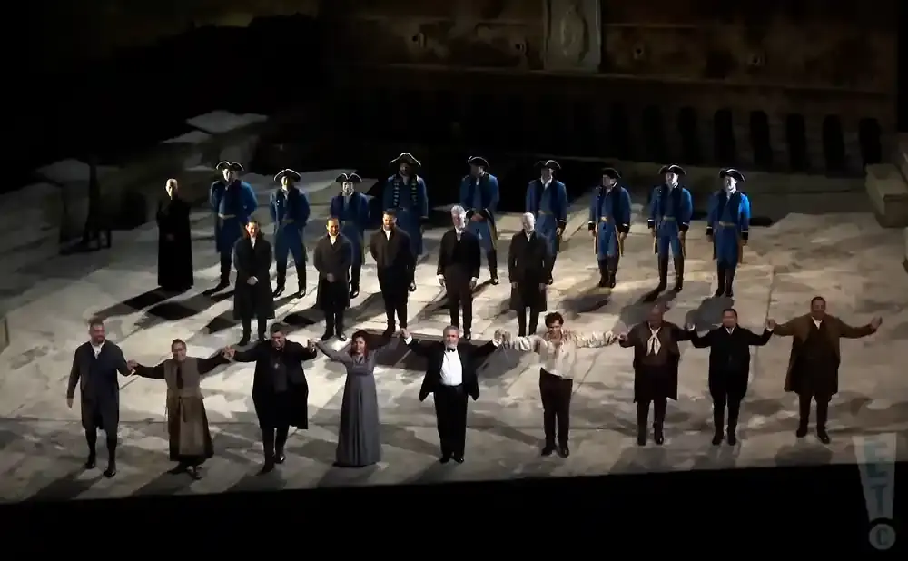 A group of performers in historical costumes stand holding hands on a stage.