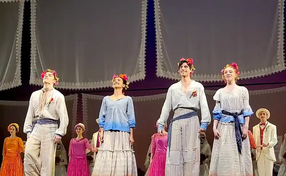 Dancers in floral headbands on stage, dressed in peasant-style clothing.