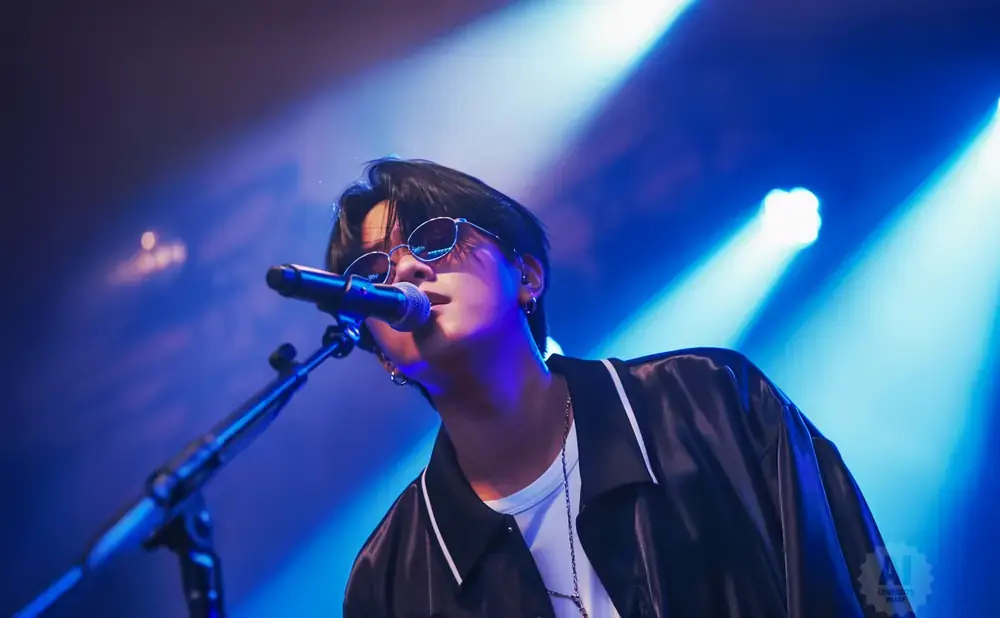 A singer with sunglasses performs on a stage with blue spotlights.