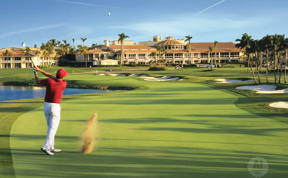 Golfer in red shirt and white pants swings club on a golf course with sand flying.
