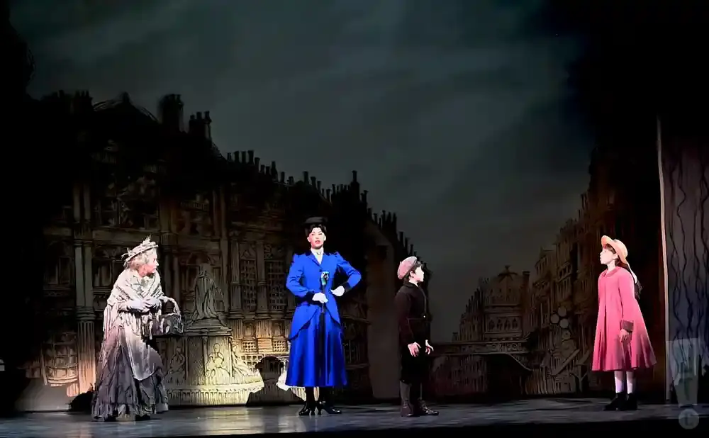 A stage production with actors dressed in Victorian-era clothing against a dark, painted cityscape backdrop.