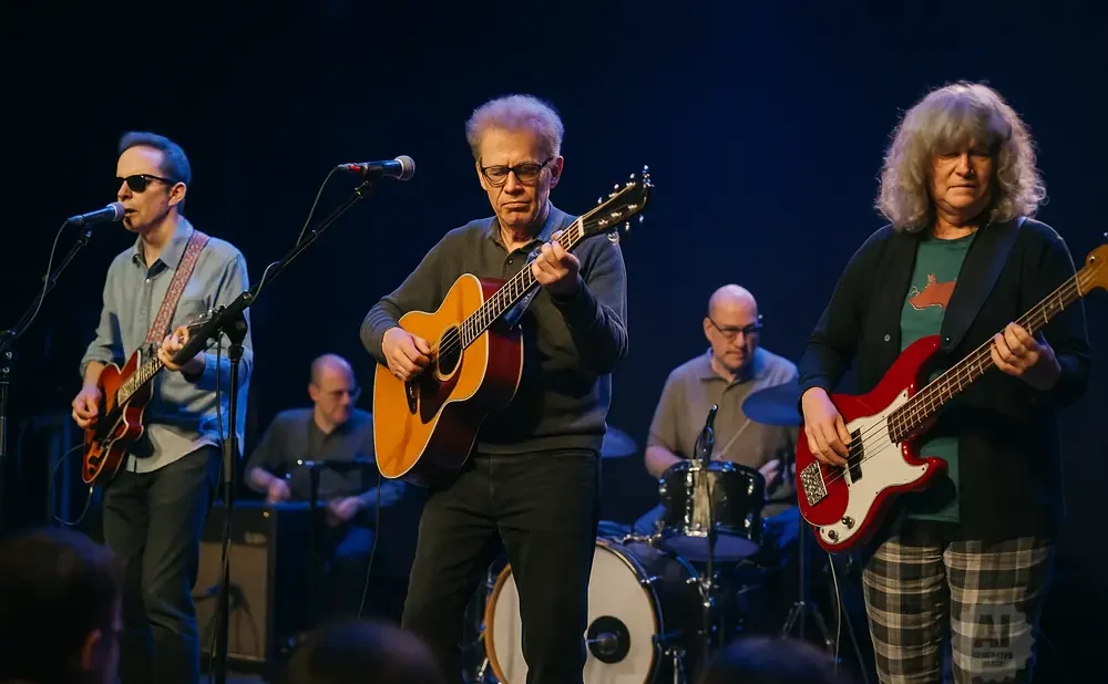 A band performs on stage with three guitarists and a drummer.