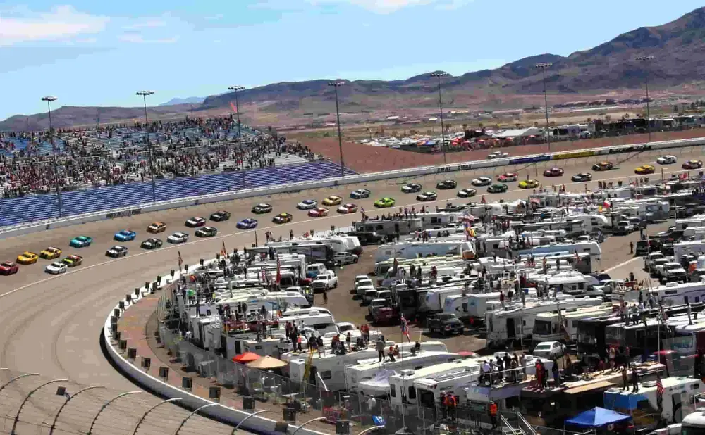 Race cars on a track with grandstands and RVs in the background.