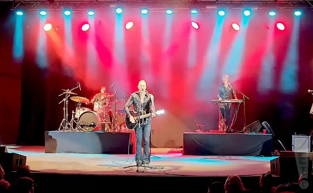 A band performs on stage with red and blue spotlights.