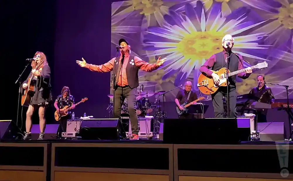 A band performs on stage with a large floral projection behind them.