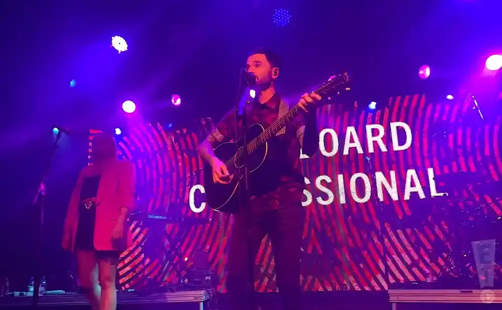 Singer with guitar on stage under purple lights with 