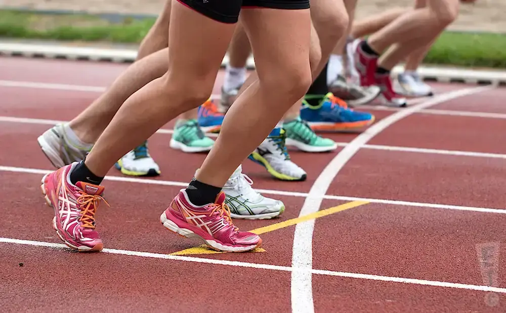 Runners' legs and colorful athletic shoes on a red track, poised for a race.