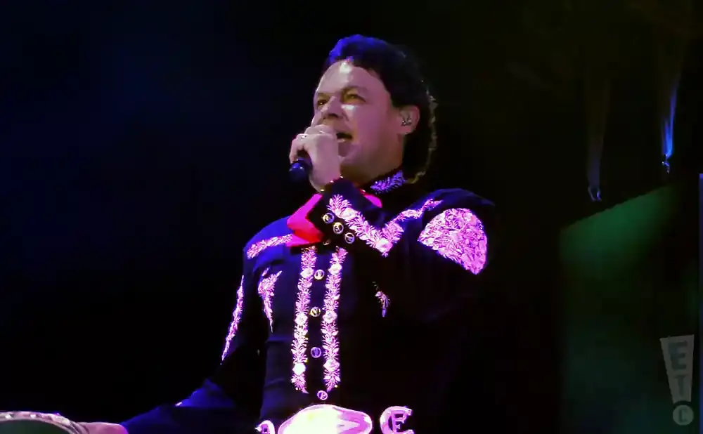 A man in a black and pink mariachi outfit sings into a microphone onstage.