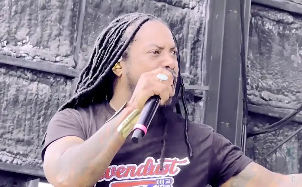 Man with dreadlocks sings into a microphone, wearing a t-shirt with 