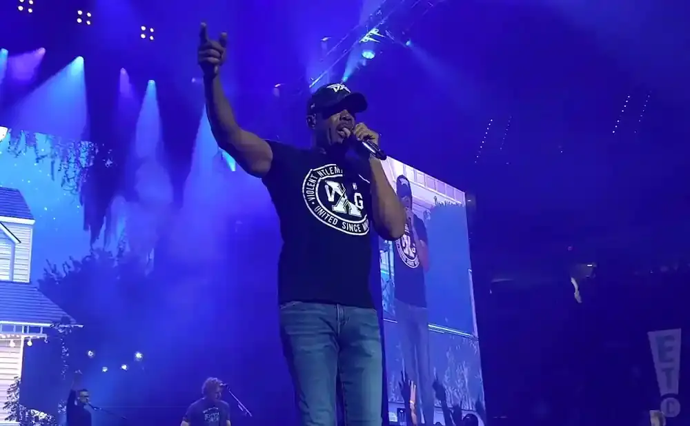 Rapper T.I. performs on stage in front of a large screen and blue lights.