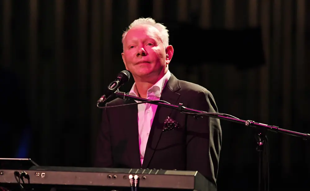 Man playing keyboard with pink lighting, wearing a suit with a polka dot pocket square.