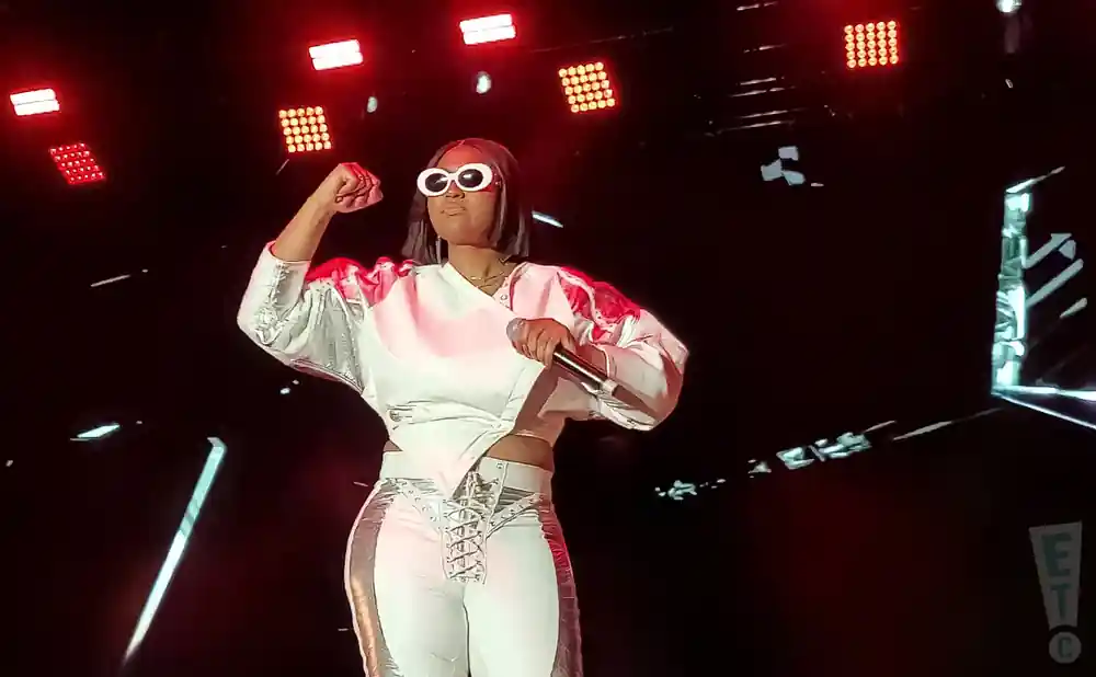 A woman performs on stage wearing a white and silver outfit and large white sunglasses.