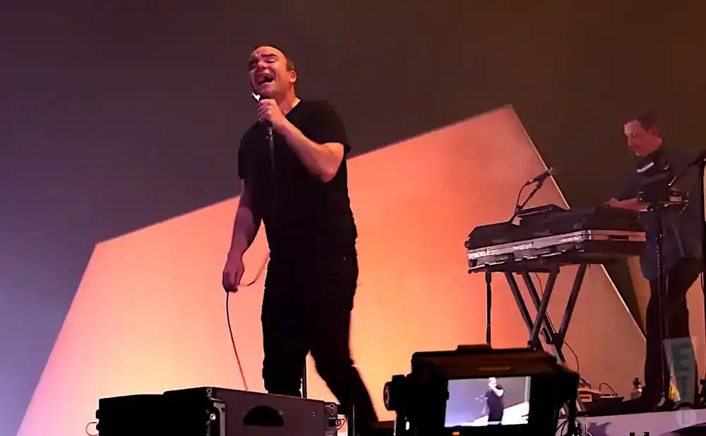 A singer on stage with a microphone, with a keyboard player in the background.