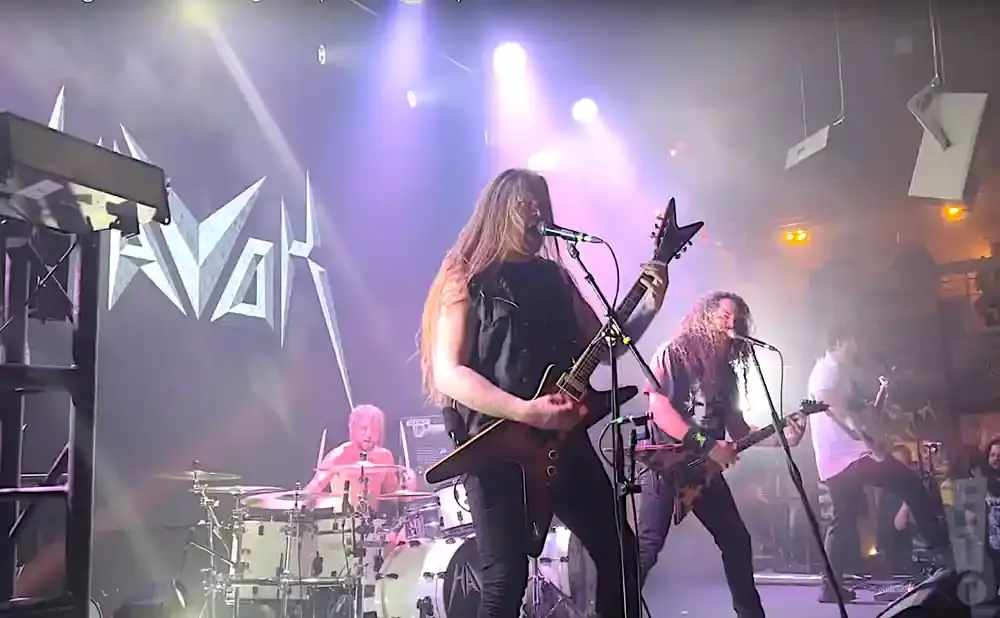 A band performs on stage with a large logo behind them.