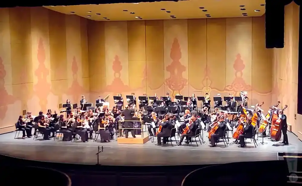 An orchestra performs on stage in front of a large, painted backdrop.