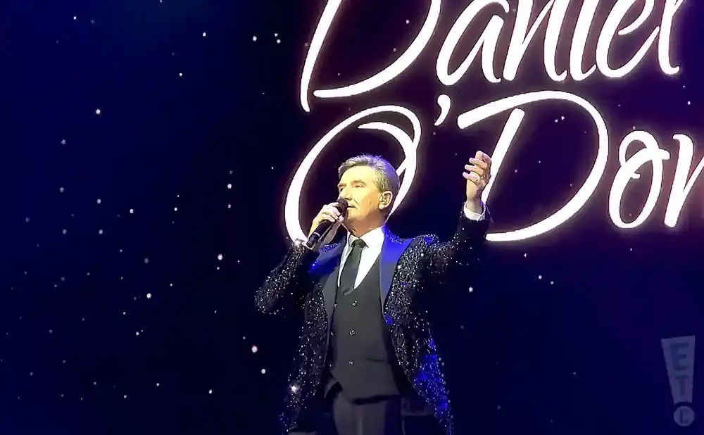 Singer Daniel O'Donnell on stage wearing a sparkly jacket and holding a microphone.