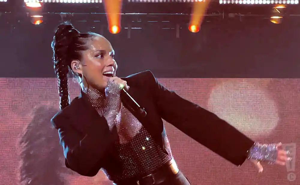 Singer Alicia Keys performs on stage, wearing a sparkly top and black blazer with her hair in a braided ponytail.