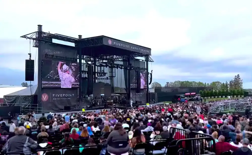An outdoor concert at FivePoint Amphitheatre with a large crowd and a band performing on stage.