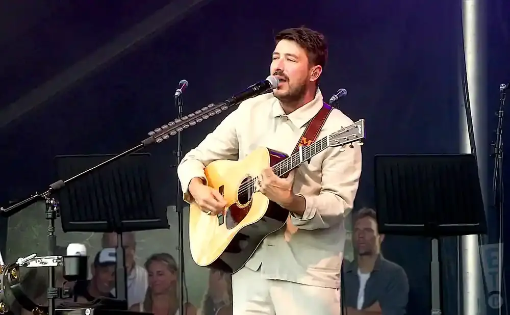 A man plays an acoustic guitar and sings into a microphone on stage.