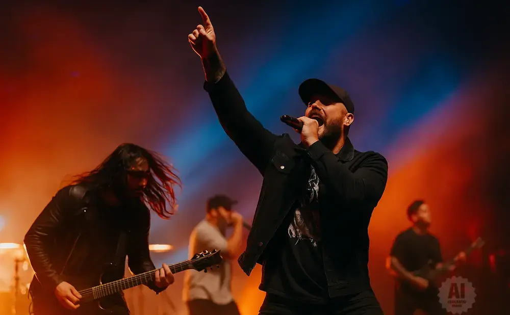 A lead singer with a microphone and arm raised at a concert, with a guitarist in the foreground.
