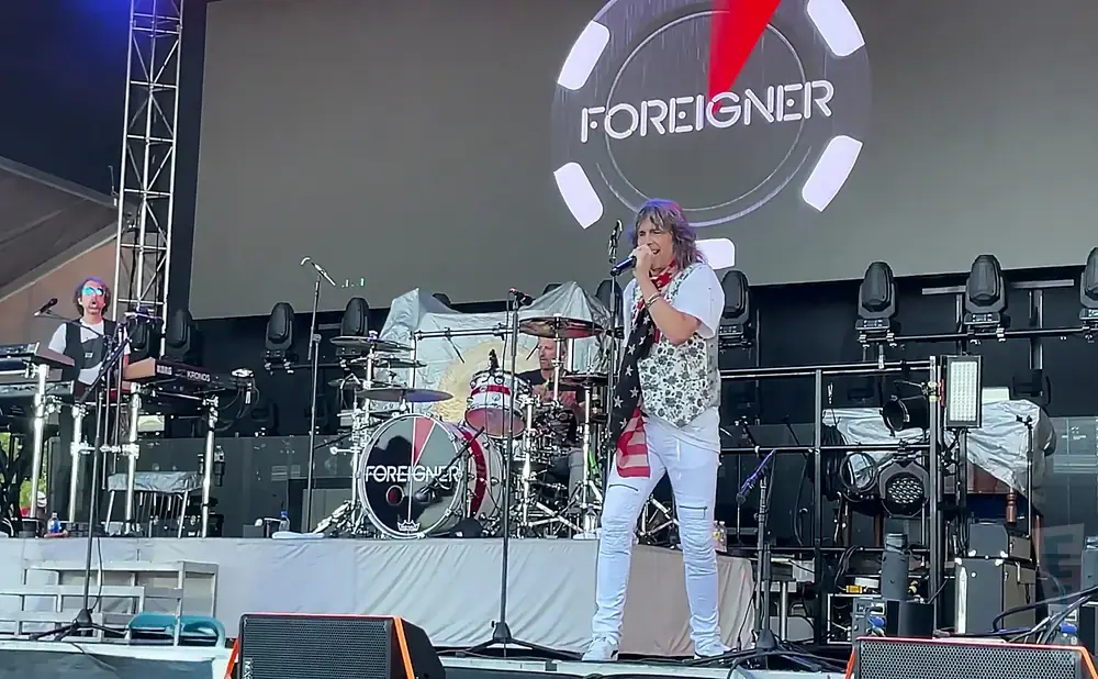 A band named Foreigner performs on stage with a singer in white pants and a patterned vest.
