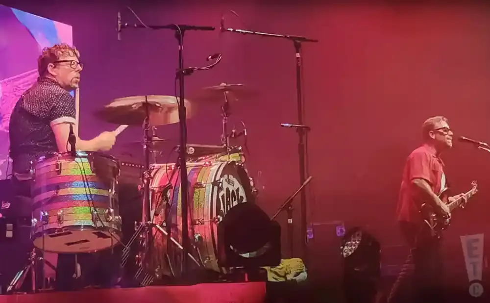 Band playing music on stage with colorful drums and a guitarist in a red shirt.