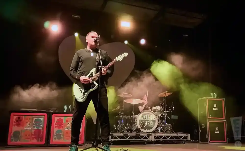 A male singer plays a light green guitar on stage with fog and green lights.